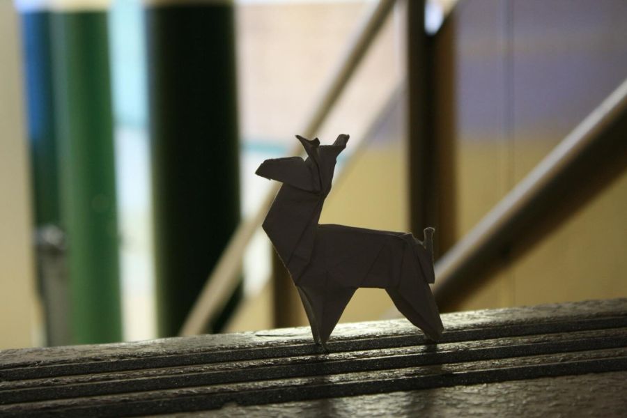 Intricate origami deer figure highlighted by indoor lighting, creating playful shadows on a textured surface.